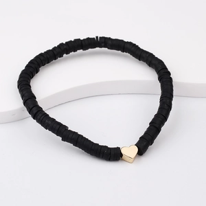 Detail of bohemian black heishi beads bracelet with a golden heart charm on a white stand
