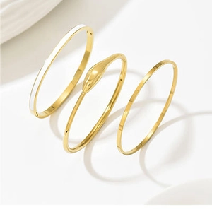 Detailed macro view of a three-piece gold-plated bracelet set with snake head and white enamel
