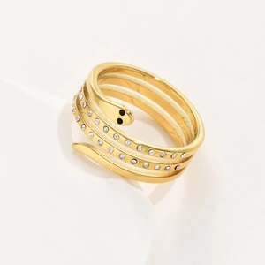Golden snake-shaped stainless steel layered ring with crystal inlay on white stone pedestal
