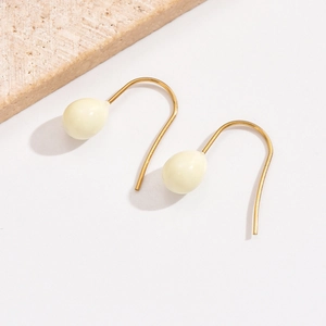 Detailaufnahme eleganter goldener Hakenohrringe mit cremefarbenen Anhängern in Ballonform