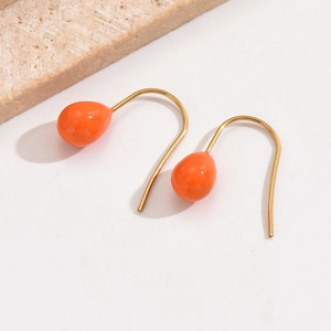 Detail von leuchtend orangen Tropfenohrringen mit Goldhaken auf minimalistischem Stein