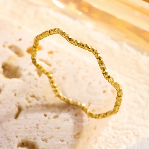 Minimalistischer goldener Wellenring mit schimmernder Textur auf steinigem Hintergrund