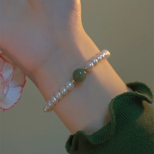Elegante pulsera de perlas con una cuenta verde y detalles dorados en la muñeca