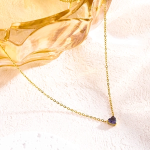 Close-up of a gold O-chain necklace with a purple heart-shaped gemstone on pink texture