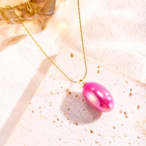 Macro detail of gold-plated chain and pink resin oval pendant on natural stone base