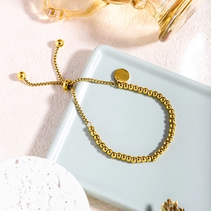 Verstelbare gouden roestvrijstalen kralenarmband met ronde hanger op een dienblad