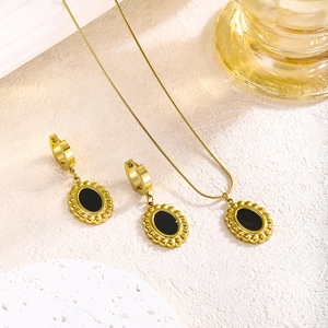 Retro gold-plated stainless steel jewelry set with black oval pendants on beige background