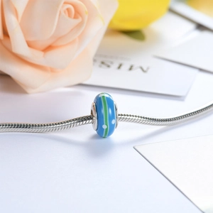 Macro shot of blue glass bead with green stripes and white dots on silver snake chain