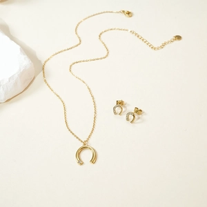 Detail shot of golden horseshoe jewelry set with necklace and earrings on stone prop