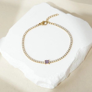Dettaglio macro di un bracciale tennis dorato con una pietra di zircone viola quadrata