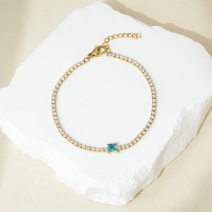 Dettaglio di un bracciale tennis dorato con piccoli cristalli e pietra blu quadrata