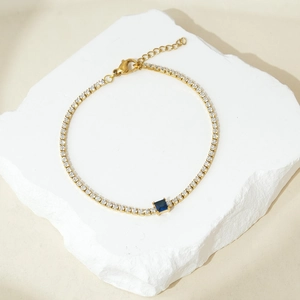 Dettaglio macro del bracciale tennis dorato con zirconi bianchi e pietra quadrata blu