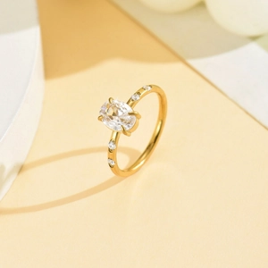 Dettaglio anello in acciaio dorato con zircone ovale centrale e pietre laterali luminose