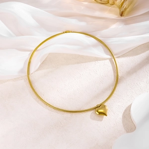 Detail of a polished gold heart pendant on a sleek snake chain over white silk fabric
