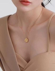 Detailed close-up of 18K gold plated necklace with embossed flower pendant on neck