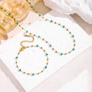Elegant stainless steel necklace set with green beads and gold accents on stone slabs