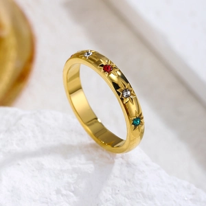 Gold ring with colorful zircon stones and starburst engraving on white stone background