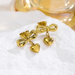 Golden bow and heart stud earrings set on white stone with elegant warm lighting