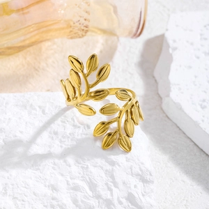 Detalle de anillo abierto dorado con diseño de hojas de olivo sobre piedra blanca