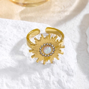 Anillo de sol calado dorado con opalo y circonitas sobre piedra blanca de textura