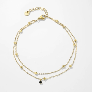 Detail of gold double-layer stainless steel anklet with beads and black zircon pendant
