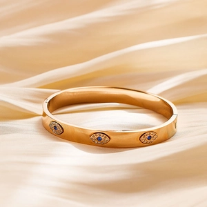 Detailed close-up of gold-plated stainless steel bangle with blue crystal evil eye motifs