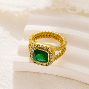 Vista de detalle de anillo con piedra verde esmeralda, banda dorada trenzada y circonitas