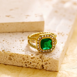 Detalle de un anillo con gema cuadrada verde, banda de oro trenzado y halo de diamantes