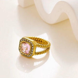 Detalle de anillo con gema rosa cuadrada, banda dorada trenzada y circonitas engastadas