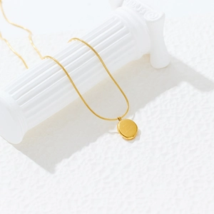 Détail d'un collier à maille serpent dorée avec pendentif rond gravé sur un pilier blanc