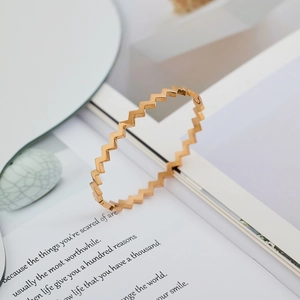 Vista detallada de un brazalete geométrico dorado en zigzag sobre fondo minimalista