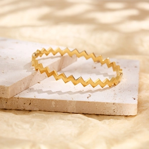 Vista macro de la pulsera ondulada de acero de titanio dorado sobre superficie de piedra