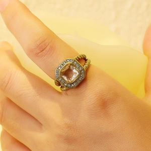Detalle de anillo dorado con circonita cuadrada y diseño de banda trenzada elegante