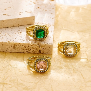 Detalle de anillos trenzados dorados con circonitas cuadradas verde esmeralda, blanca y rosa