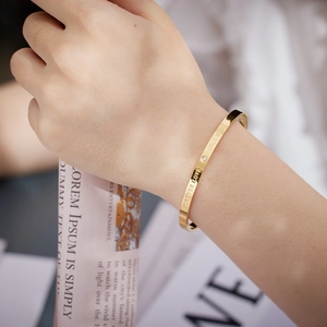 Dettaglio del bracciale rigido dorato con scritte incise e una pietra di zircone lucido