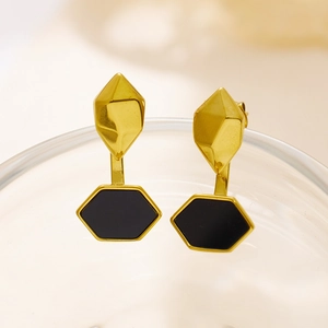 Detailed view of geometric gold earrings with black hexagonal drops on glass rim