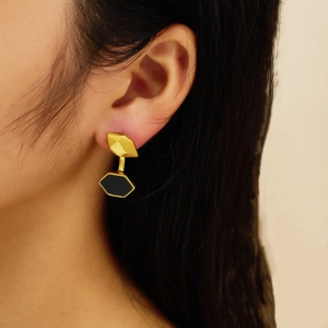 Close-up of elegant gold geometric earrings with black hexagonal drops worn by a model