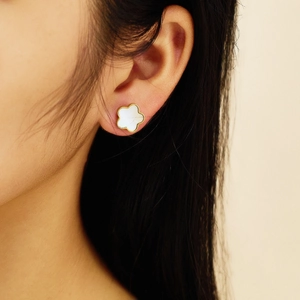 Detail of elegant gold clover earrings with white mother of pearl inlay on model
