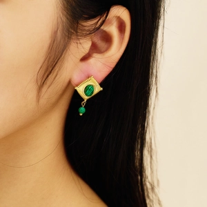 Detailopname van vintage gouden oorbellen met groene malachietsteen op een model