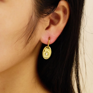 Close-up of a gold titanium hoop earring with a pearl coin pendant on a female model