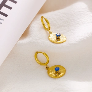 Close-up of golden hoop earrings with hammered metal discs and blue gemstones