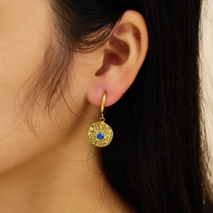 Detail of 18k gold earrings with hammered texture and a brilliant blue gemstone