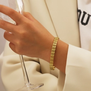 Gros plan d'un bracelet manchette doré évidé porté par un mannequin avec un verre