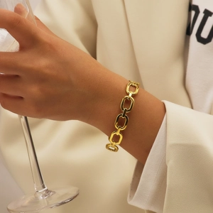 Gros plan d'un bracelet à maillons ovales dorés polis porté par un mannequin en extérieur