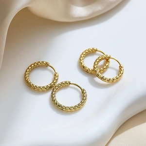 Detail of gold titanium hoop earrings with textured scale pattern on champagne silk