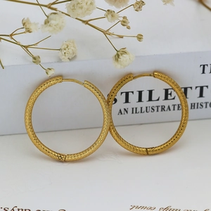 Detailed view of large gold hoop earrings with intricate diamond texture on white book