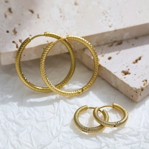 Macro detail of gold titanium steel hoop earrings with textured knurled pattern design