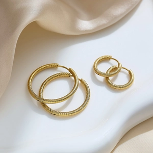 Golden stainless steel hoop earrings with textured diamond-cut finish on ceramic tray