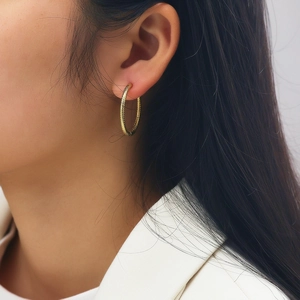 Close-up of gold hoop earrings with textured finish worn by a model in a side view