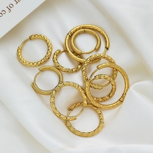 Gold titanium steel hoop earrings with textured patterns on white silk fabric background